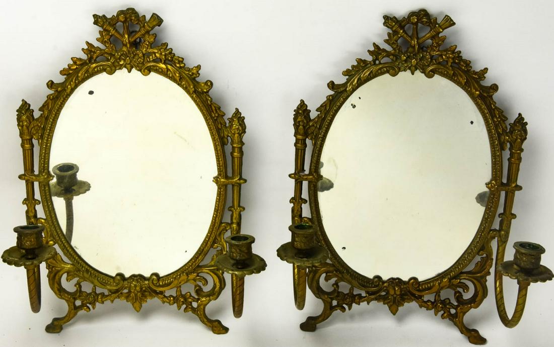 Pair Brass Neoclassical Style Mirrored Sconces: Pair Brass Neoclassical Style Mirrored Sconces. Pair of Neoclassical sconces with mirrors and two arms, each with crossed torch, bow and floral motifs. Each measures 16 inches x 10 inches x 6 inches.