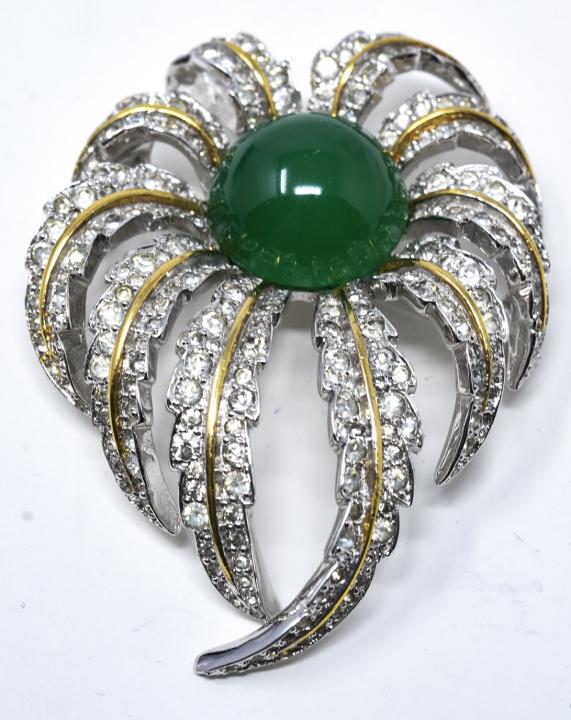 Jomaz Rhodium Faux Jadeite Brooch / Pin: Jomaz Rhodium Faux Jadeite Brooch / Pin. Rhodium brooch with clear paste and center faux jadeite cabochon signed Jomaz. Measures 2.5 inches in length.