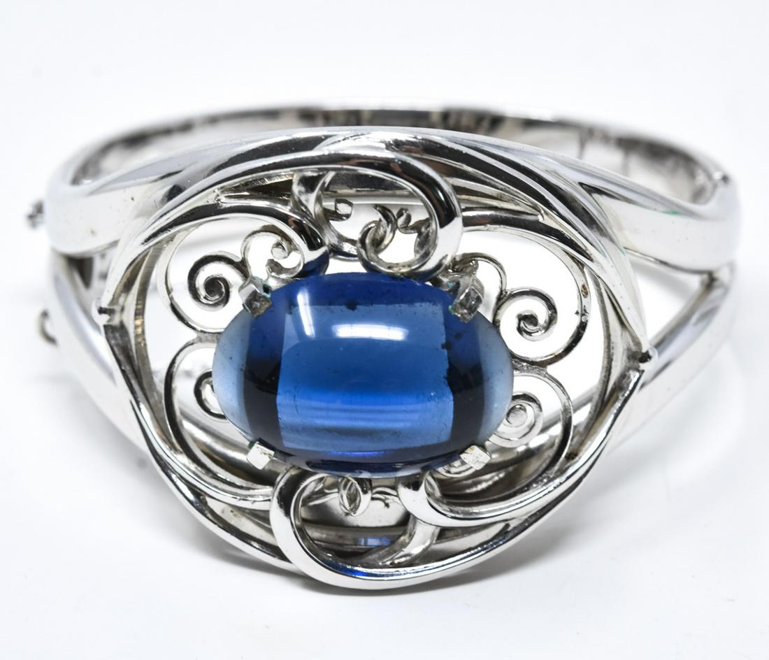 C 1960 Whiting & Davis Rhodium Bangle Bracelet: C 1960 Whiting & Davis Rhodium Bangle Bracelet. Rhodium split bangle bracelet with swirly openwork and large faux sapphire oval cabochon. Marked on interior. Measures 2.5 inches across the interior op
