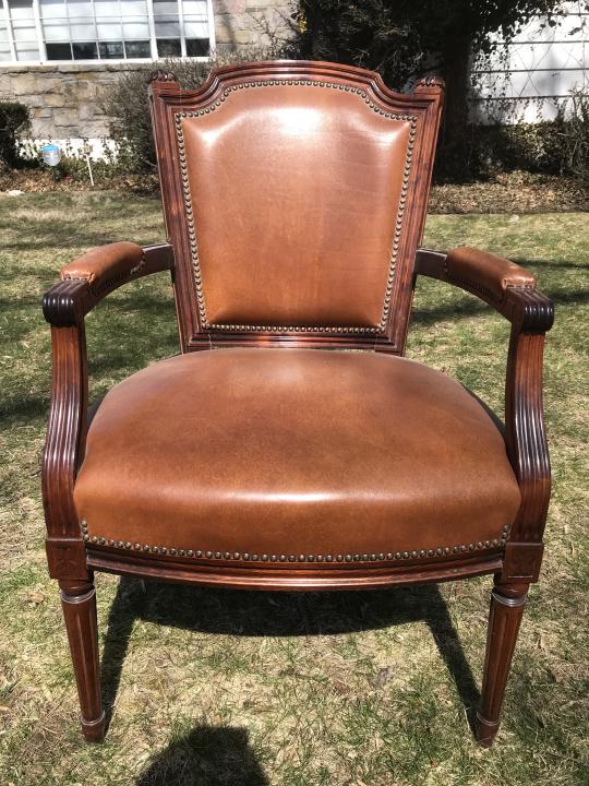 Louis XVI Carved Leather Upholstered Armchair: Louis XVI Style Carved Leather Upholstered Armchair. Leather upholstered with leather pads to arms and nailhead trim. Fluted frame engraved with rosettes at corners, legs resting upon arrow feet. Meas