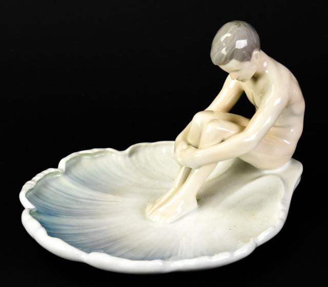B&G Porcelain Figural Nude Boy on Lily Pad Dish: B&G (Bing & Grondahl) Denmark Porcelain Figural Nude Boy on Lily Pad Dish. Marked on bottom B&G Kjobenhavn, Denmark. Measures 6 inches high x 7.5 inches wide x 8.5 inches deep.