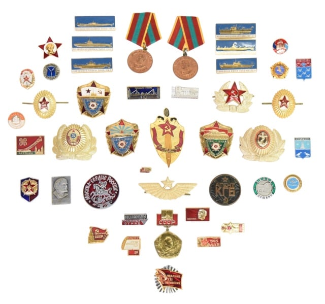 Assorted Collection of Military Badges & Hat Pins: Assorted Collection of Soviet and Russian - Era Military Badges, Commemorative Medals, and Hat Pins in a Display case.The case contains various metallic and enameled insignia, including naval ship bad