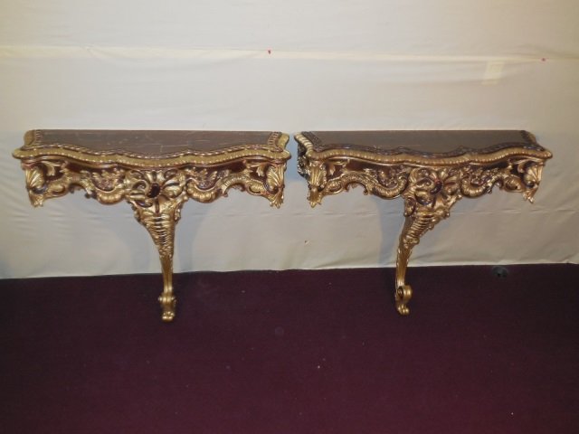 Pr. of Gilt Wood Wall Mount Console Tables: A pair of gilt wood wall mount console tables. Heavily carved single leg base. 40 5/8" W x 13 3/4" D x 33" H. With heavily scratched top surface, needs restoration.