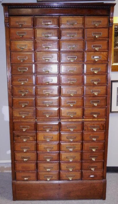 Antique Walnut Library "Shannon Filing Cabinet": Antique Irish walnut "Shannon Filing Cabinet" with 60 drawers and two pull out shelves. Brass pulls featuring the Shannon monogram. 46 1/2" W 17 7/8" D x 88 3/4" H. The bottom left and right drawer pu