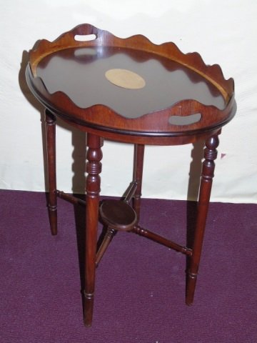 Mahogany Butler Tray Table from The Federalist: An oval mahogany butler tray table from the Federalist (Greenwich, CT) with scalloped gallery, light wood banding on outside edge and center oval brass plaque. 27" W x 18" D x 23 1/4" H. Very good con