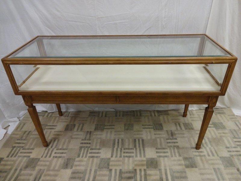 Jansen Natural Wood & Beveled Glass Showcase: A Jansen natural wood and beveled glass showcase with a decorative design on legs. Front glass panel opens downward. 60 1/2" W x 22 3/4" D x 36" H.