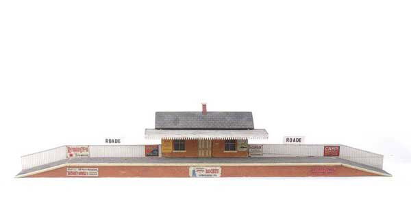 Bassett-Lowke O Gauge Station "ROADE": Bassett-Lowke O Gauge Station "ROADE" measuring 35" x 3 1/2" with a central building measuring 9" x 3 1/2" approx. Finished in grey, brown with white mack fencing and a number of enamels signs attache