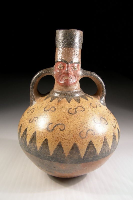 Wari (Huari) Painted Jar: A Huari (Wari) jar with a human head, Ca. 800 A.D. This classic Huari jar has a human face on the spout, with two handles coming from the spout to the body. At the base of the spout is painted a large