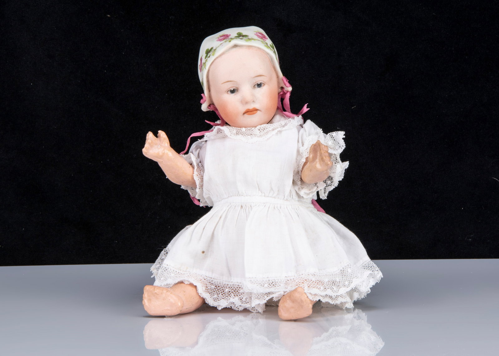 A small Gebruder Heubach Baby Stuart,: A small Gebruder Heubach Baby Stuart, with blue intaglio eyes, a closed downturned mouth, moulded white bonnet with two ribbon tie-holes and pink rose transfer decoration, back of head with HEUBACH in