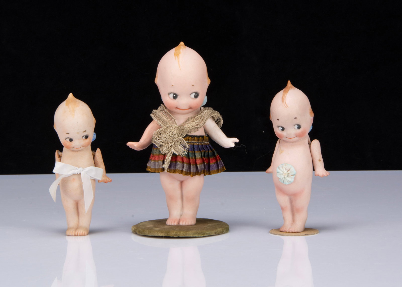 Three Rose O’Neill all-bisque Kewpie,: Three Rose O’Neill all-bisque Kewpie, all with black painted side glancing eyes, smiling mouths, blonde painted tufts of hair, blue wing buds and jointed arms, the largest wearing a kilt and mou