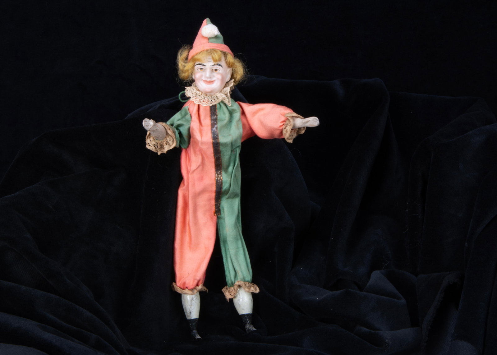 An unusual bisque headed squeak toy clown,: An unusual bisque headed squeak toy clown, with heavy Mr Punch type features with brown painted eyes and black brows, blonde wig, back of head indistinctly impressed, painted wooden limbs, pink and gr
