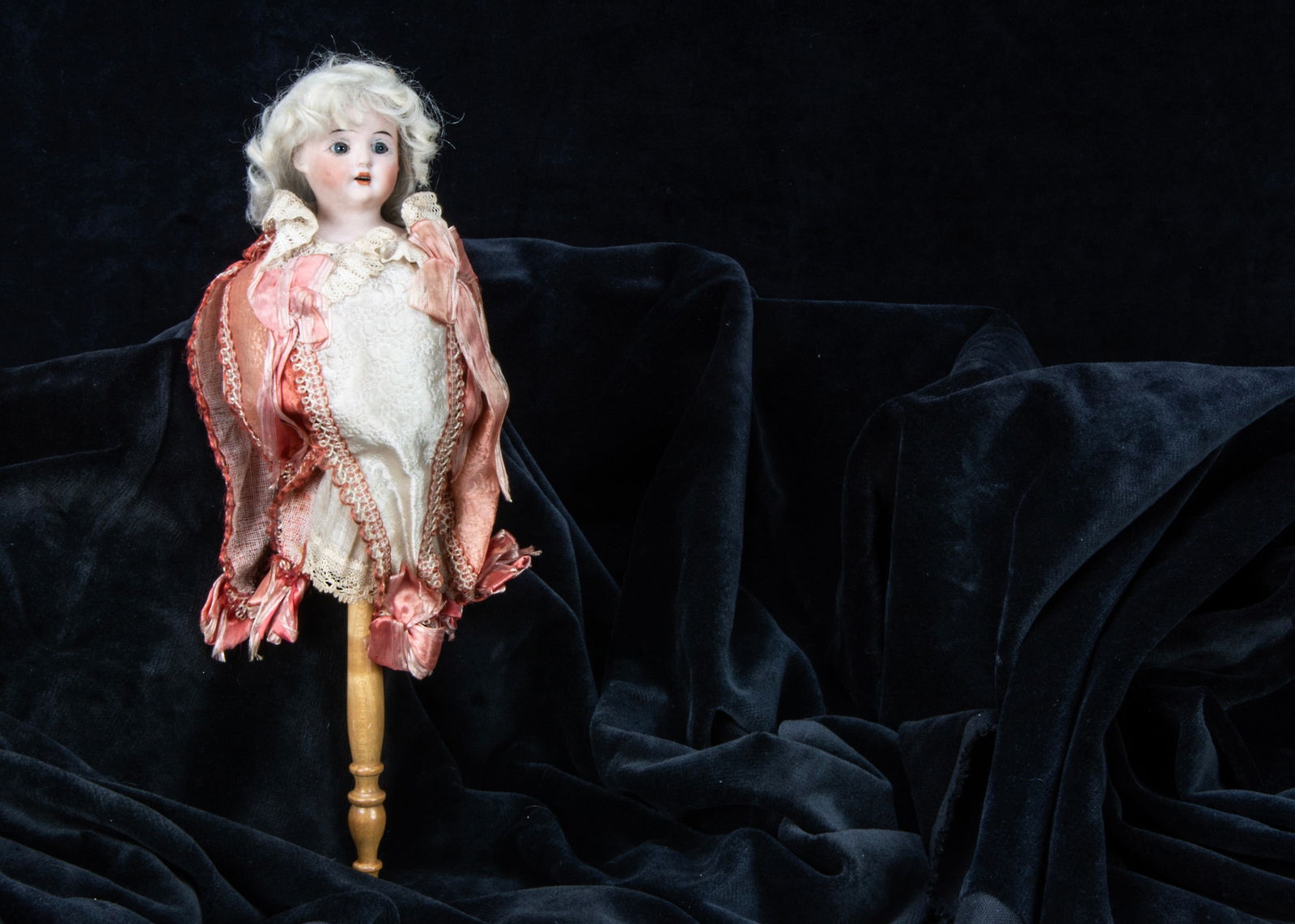 A bisque headed musical marotte,: A bisque headed musical marotte, with Schoenau & Hoffmeister shoulder head, white mohair wig, pink and cream pointed collar, turned wooden handle, when spun music plays —13in. (33cm.) high