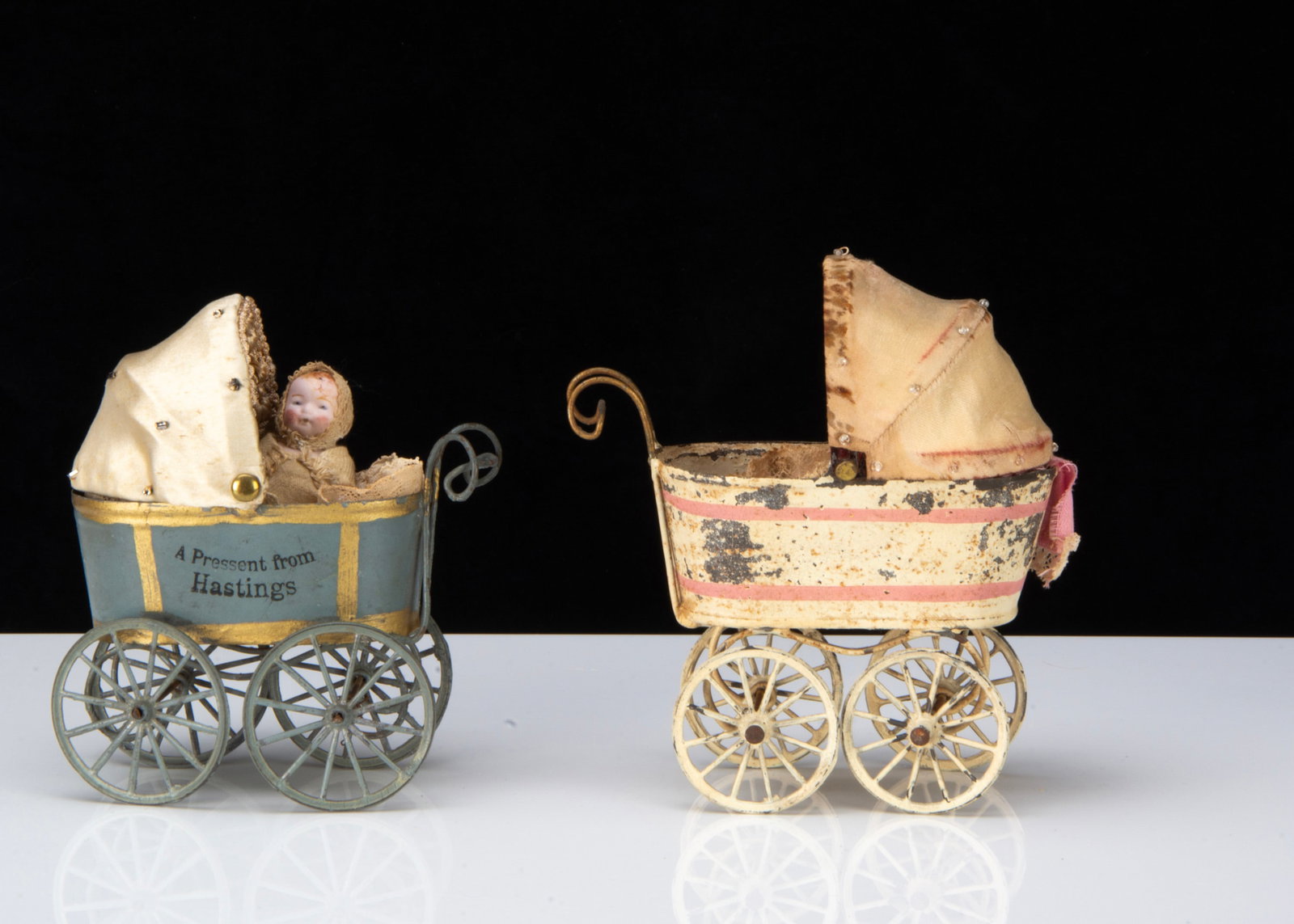 Two tinplate dolls or larger dolls’ house perambulators,: Two tinplate dolls or larger dolls’ house perambulators, one painted blue and gold with soft metal wheels, the side stamped ‘A Present from Hastings’ with all-bisque baby —4in.