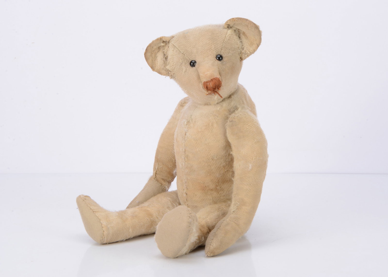 An early white mohair teddy bear,: An early white mohair teddy bear, possibly Hecla, black boot button eyes, brown stitched nose, swivel head, jointed limbs and hump ó19 Ωin. (49.5cm.) high (bald, small hole to top of muzzle,