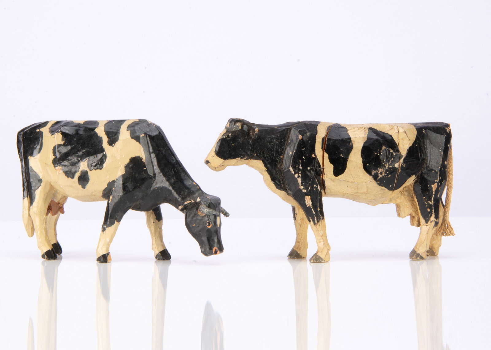 Two Forest Toys of Brockenhurst standing cows,: Two Forest Toys of Brockenhurst standing cows, wooden, black and white with lead horns, one grazing, one with string tail ó6in. (15cm.) long (non-grazing with some cracking)