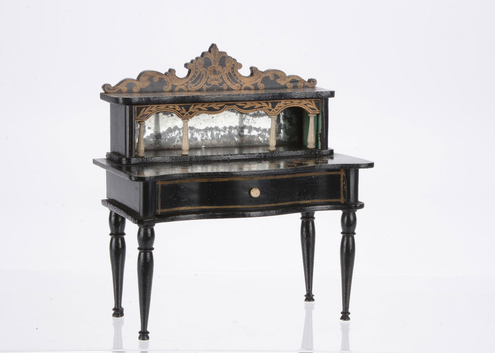A Waltershausen dolls’ house desk,: A Waltershausen dolls’ house desk, with unusual black finish, gilt transfer decoration, shelf with bone column supports and drawer with bone handle —4 ½in. (11.5cm.) wide