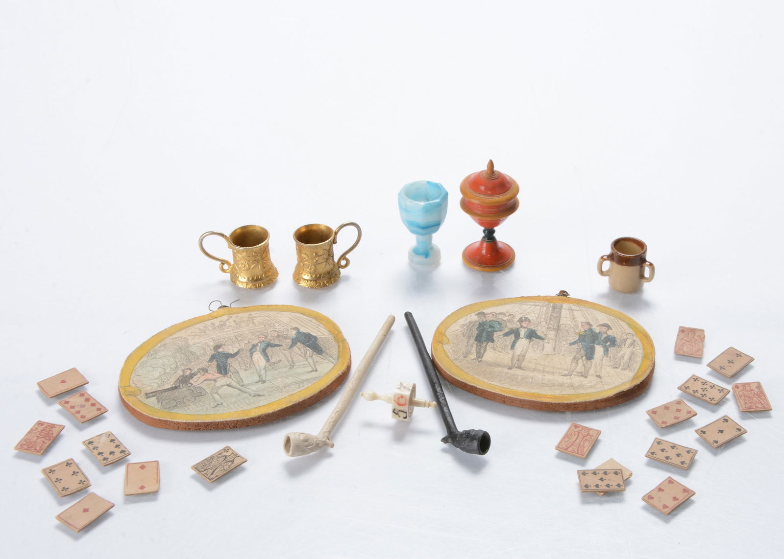 Dolls’ house chattels,: Dolls’ house chattels, a bone teetotum —¾in. (2cm.) high, two clay pipes, a turned and painted wooden challis, some playing cards, two gilt metal cups, a blue slag glass glass, a ston