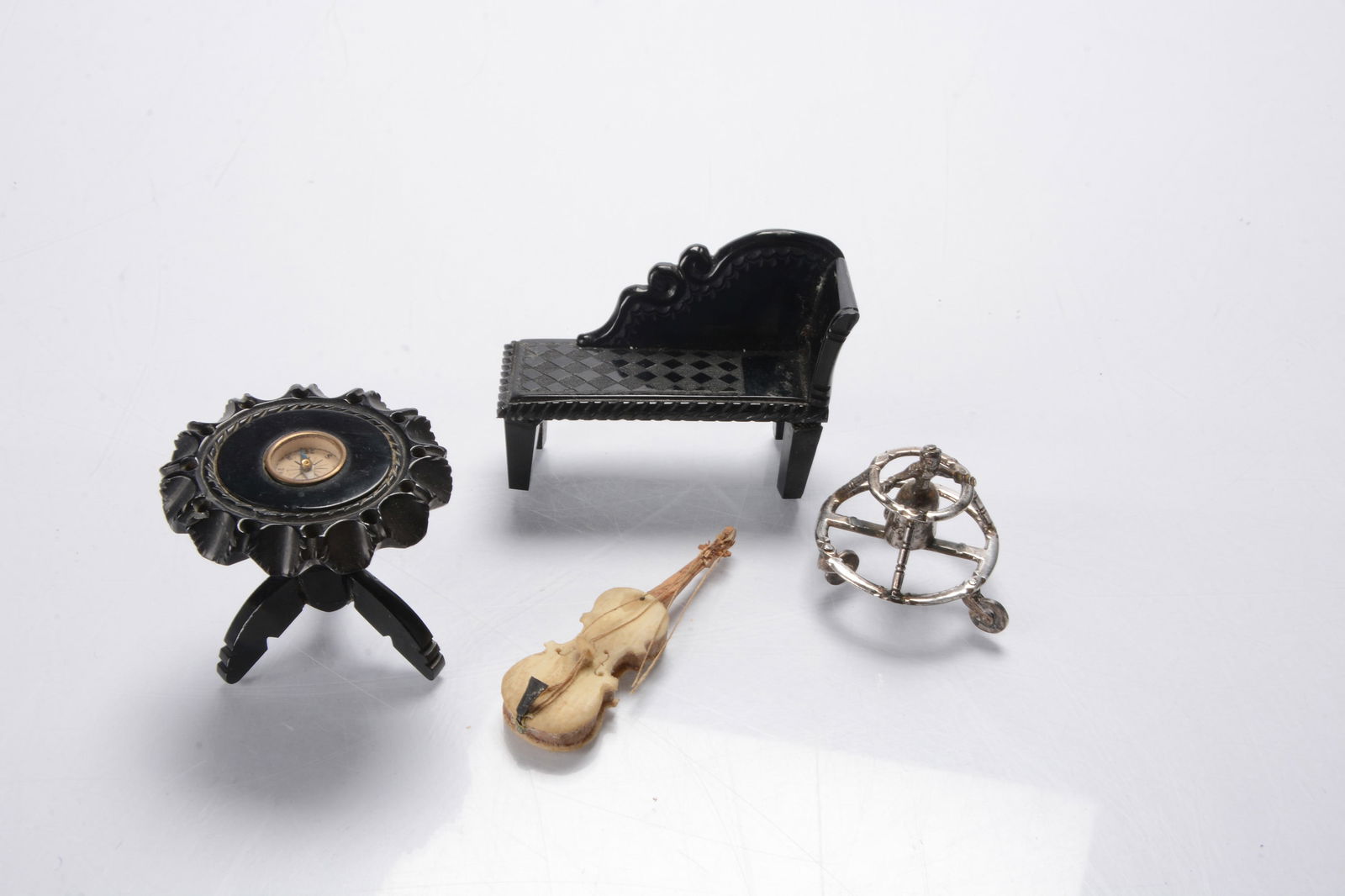 A continental silver dolls’ house baby in walker,: A continental silver dolls’ house baby in walker, the figure in dress and three castors —1 ½in. (4cm.) high, a Whitby jet carved tripod table inset with compass and chaise longue; and
