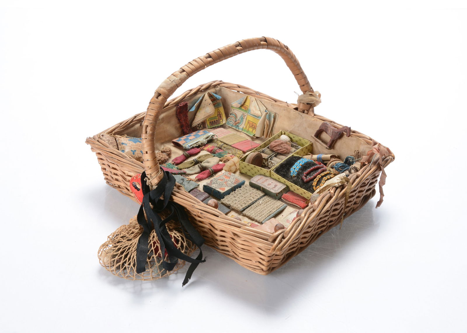 A large size 19th century doll’s pedlar basket,: A large size 19th century doll’s pedlar basket, with goods including five wooden dolls, two packs of playing cards, six miser purses, needle cases, ribbons, balls of yarn, a wooden hose and pin