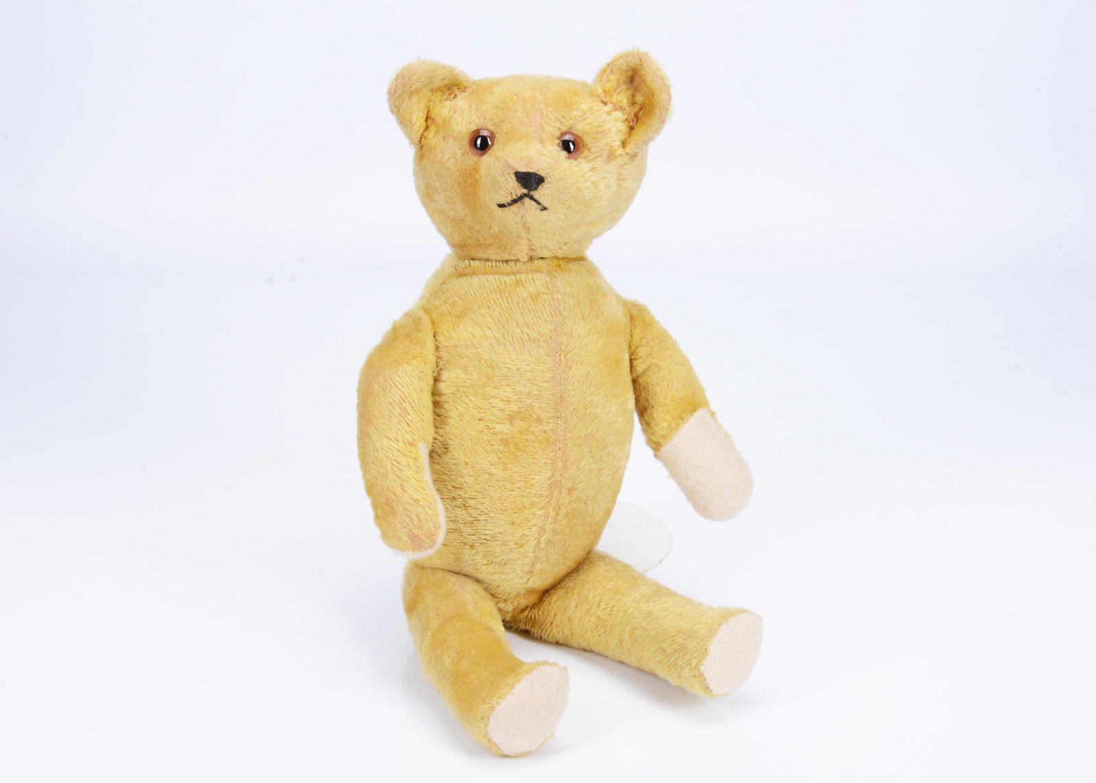 A 1920s American teddy bear,: A 1920s American teddy bear, with golden mohair, clear and black glass eyes, with painted back, black stitched nose and mouth, swivel head, jointed limbs and inoperative voice mechanism --22in. (56cm.