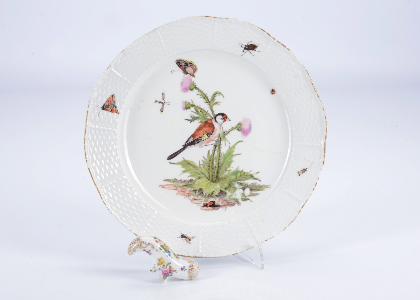 A Meissen plate painted with a goldfinch on a thistle, 1740s,: A Meissen plate painted with a goldfinch on a thistle, 1740s, with various insects, moulded basket rim and crossed sword mark —9 1/2in. (24cm.) wide (chip to rim either end of a crack across the