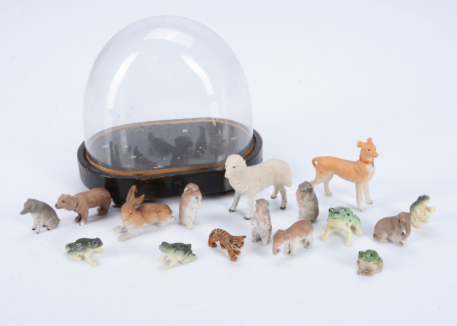 A small glass dome containing a selection of German bisque animals,: A small glass dome containing a selection of German bisque animals, including a nodding bear, a large sight hound —2in. (5cm.) long, five frogs, five elephants and others, one composition tiger