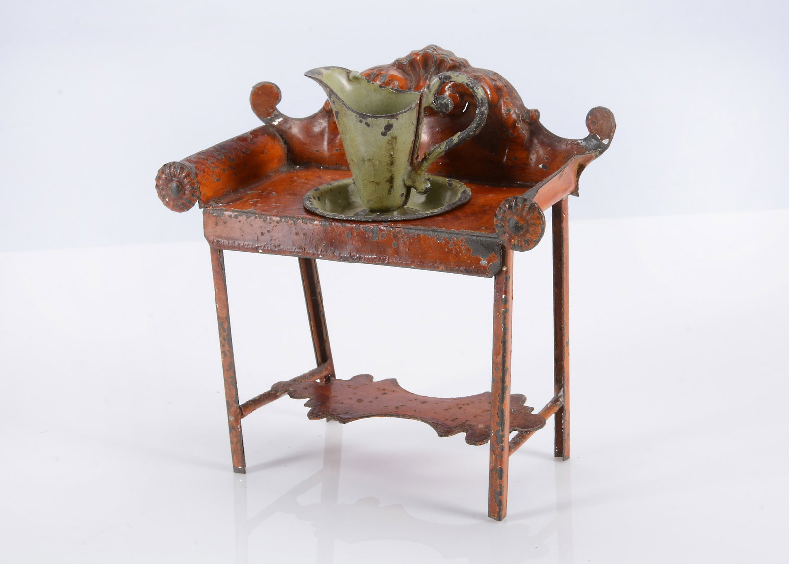 An 19th century Evans and Cartwright painted tinplate dolls’ house washstand,: An 19th century Evans and Cartwright painted tinplate dolls’ house washstand, with wood grain finish, scrolling foliage and shell back, rosette to each side of front and original green painted t