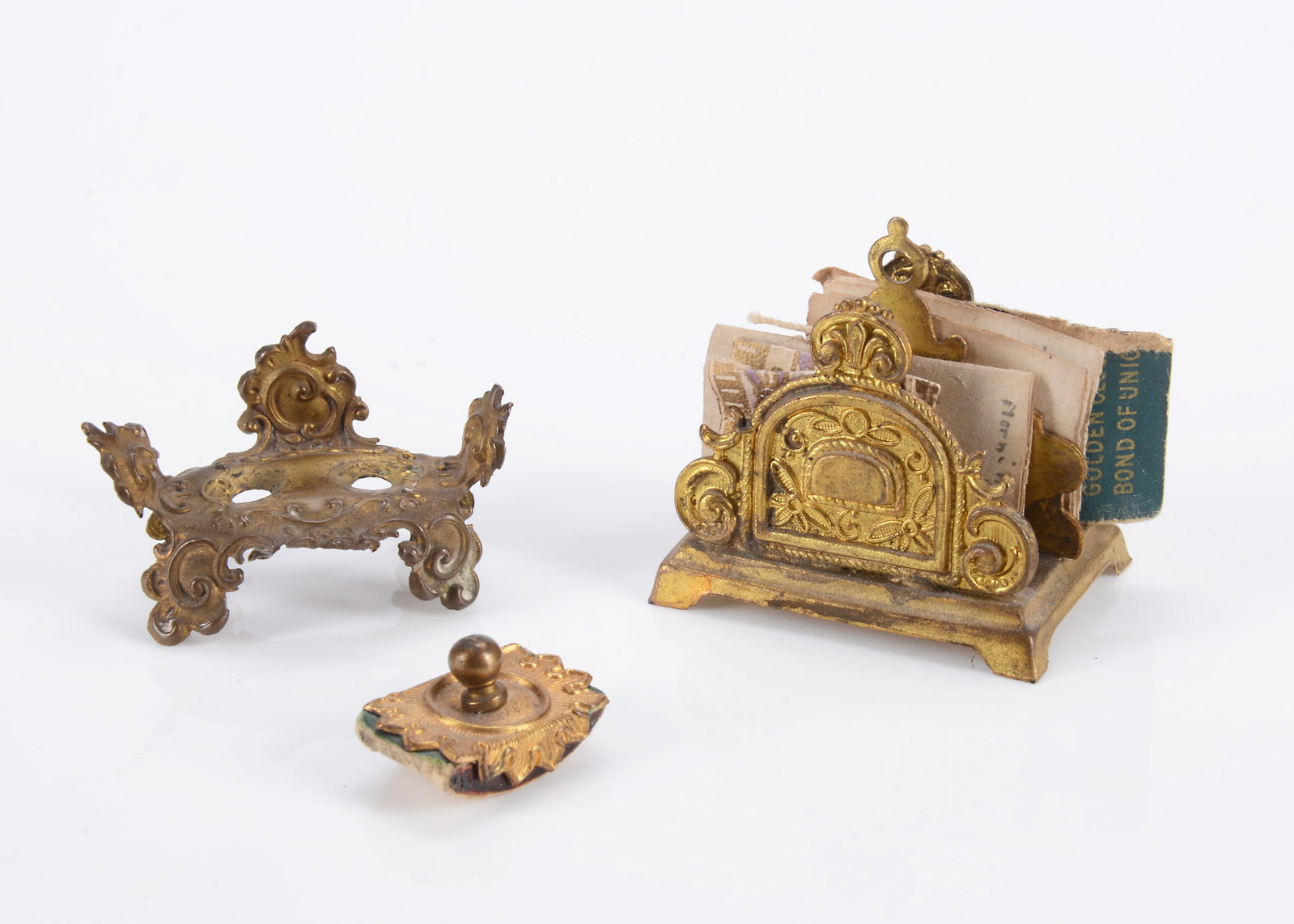 German gilt metal dolls’ house desk accessories,: German gilt metal dolls’ house desk accessories, a letter rack —1 3/4in. (4.5cm.) wide, a blotter and inkwell (missing glass wells)