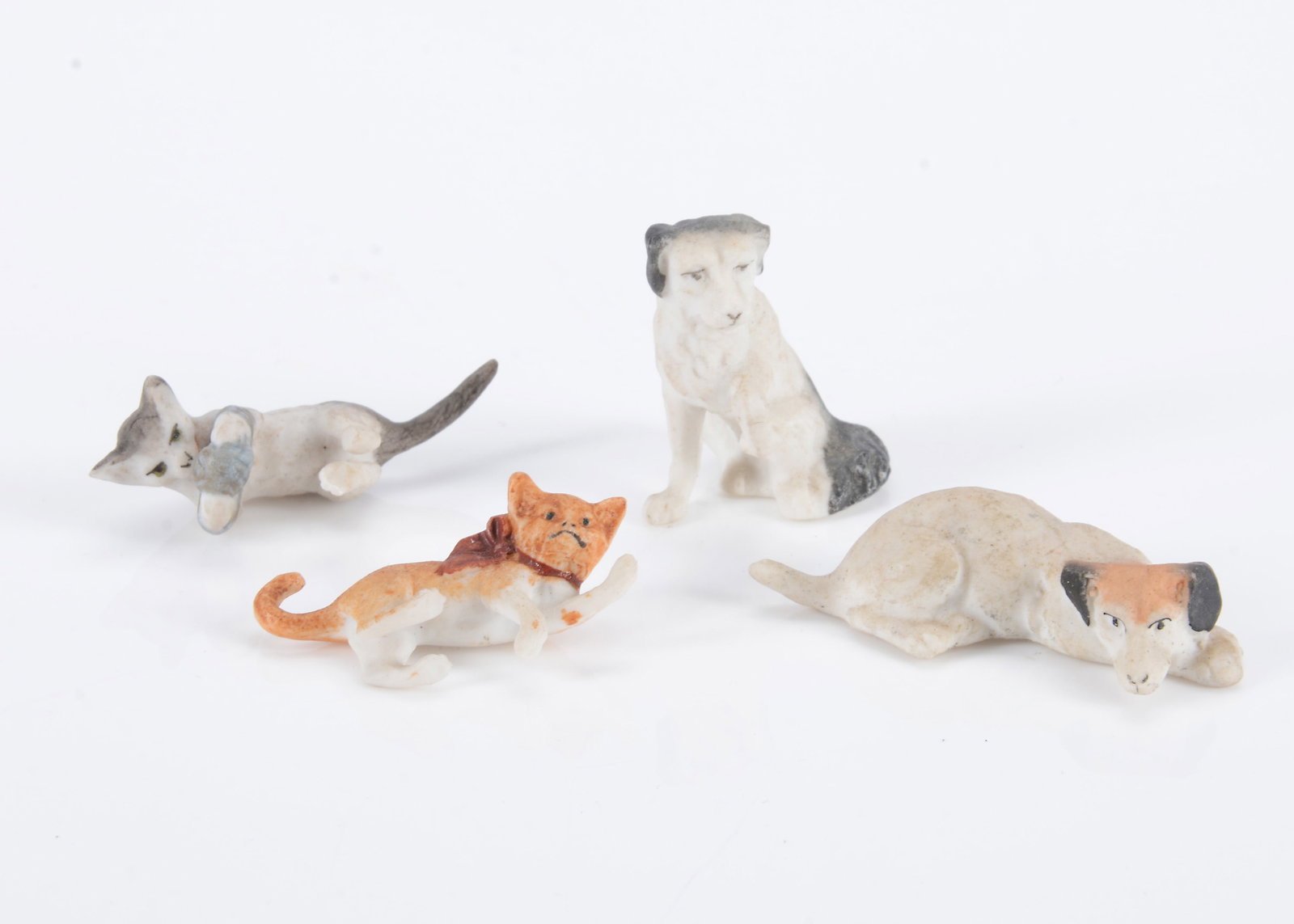 Four German bisque dolls’ house cats and dogs,: Four German bisque dolls’ house cats and dogs, two playing kittens, one ginger with red bow —1 1/4in. (4cm.) long, a grey kitten playing with a ball of wool (missing one foot), a seated sp