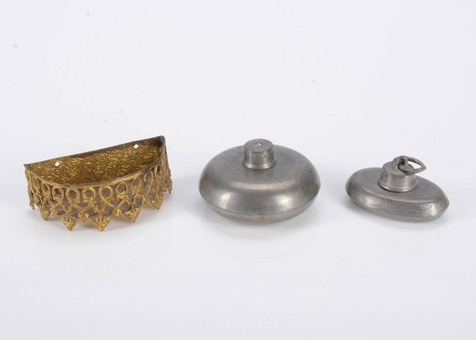 Two 19th century dolls’ house pewter bed warming pans,: Two 19th century dolls’ house pewter bed warming pans, one oval —1 3/4in. (4.5cm.) long and a circular example; and a gold painted soft metal semi circular wall mounted object, possibly a 