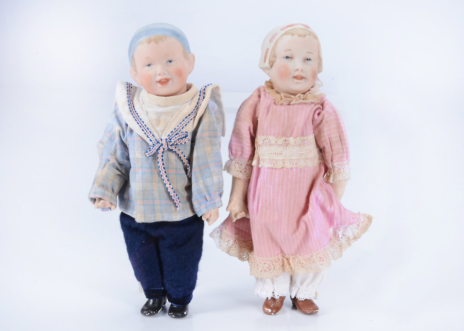 A pair of Recknagel bisque headed character dolls,: A pair of Recknagel bisque headed character dolls, with blue painted eyes, open/closed mouth with two top teeth, the girl with moulded bonnet with pink ribbon and the boy with moulded blue wool hat, j
