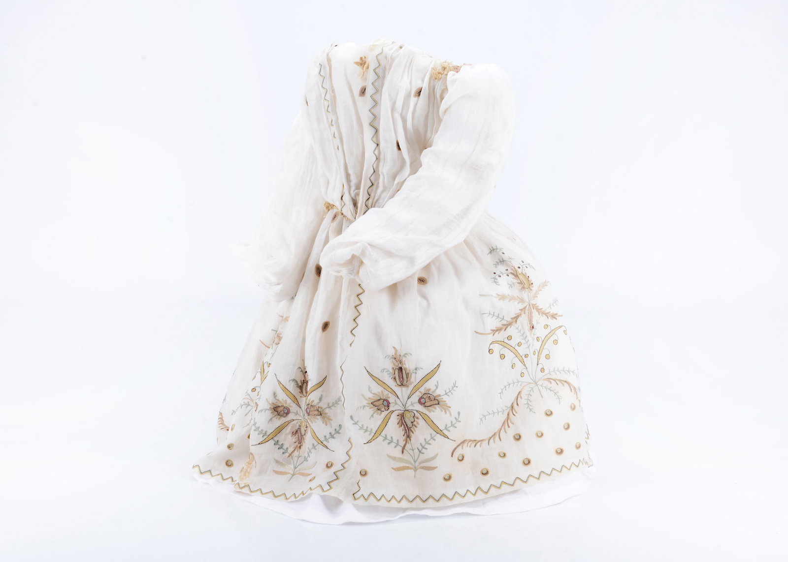 A dolls ensemble from an 18th century doll,: A dolls ensemble from an 18th century doll, white long sleeved sheer muslin dress with intricately stitched floral, spot and zigzag embroidery in yellow, green browns and blue, boned to front panel, w