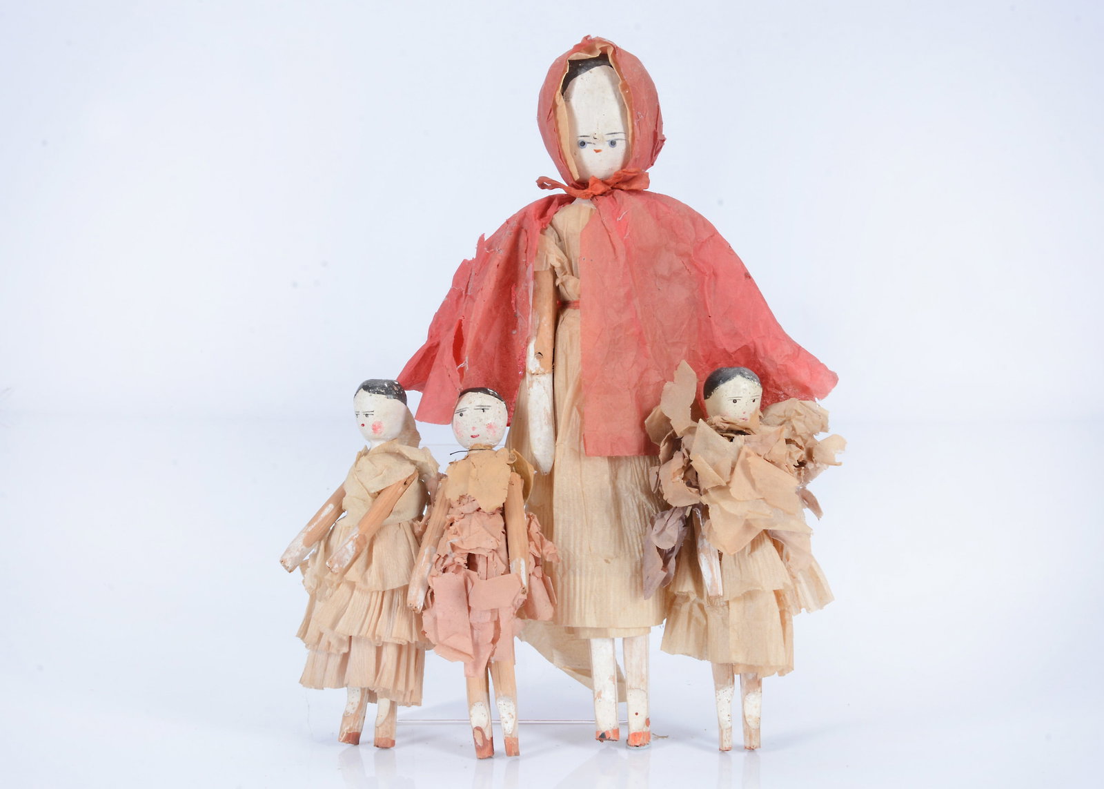 Four German peg wooden dolls, circa 1900,: Four German peg wooden dolls, circa 1900, with blue painted eyes, black centre-parted hair, jointed wooden bodies with white washed lower limbs and red shoes, the larger with inserted nose and dress a