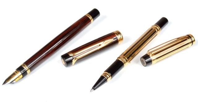 Two Waterman Pens: (1) Fountain pen with faux wood finish, 18K gold nib; (2) Gold ballpoint pen.