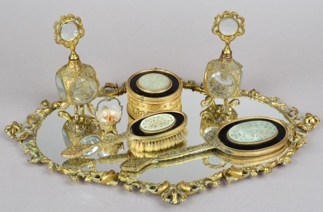 Seven Piece Woman's Vanity Set: Comprising a mirrored tray, hand mirror, hair brush, basket, and two covered perfume bottles. Tray, 25 x 16 inches.