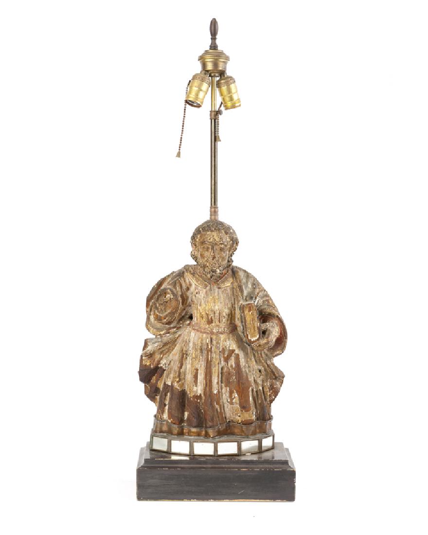 A carved and polychrome-painted wood santos lamp: 19th century and later Apparently unmarked Standing saint with book, drilled and fitted as a lamp and raised on a mirrored and beveled wood base Overall: 33" H x 10.75" W x 5.75" D