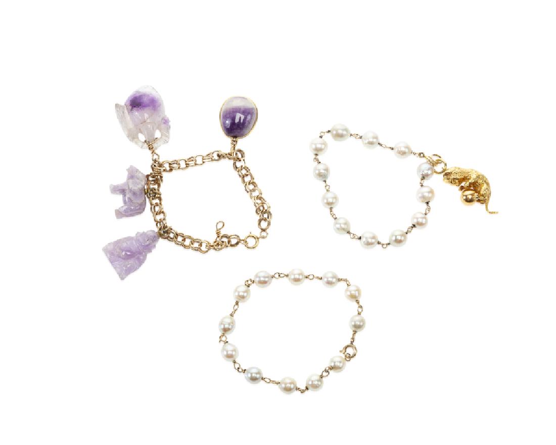 Three bracelets: 14K yellow gold Including two gold link bracelets set with cultured pearls, one suspending an 18K yellow gold cat charm; and one link bracelet suspending four varied carved amethyst charms 77.4 grams