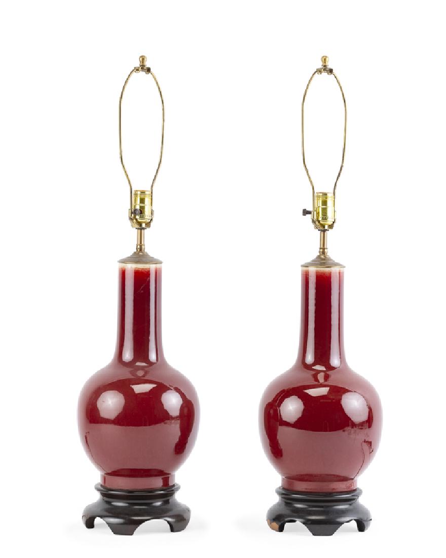 A pair of Chinese oxblood porcelain lamps: Second half 20th century Each with a long cylindrical neck over a bulbous body, on a wood base, 2 pieces Each including harp: 33.75" H x 8" Dia.