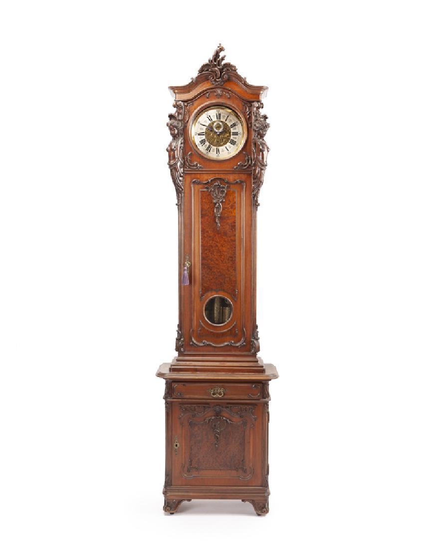 An Austrian tall case clock: Late 19th/early 20th century Dial signed: Johann Tyrichter Wien The carved wood case surmounted by a rocaille flourish over a tall rectangular case flanked by two semi-nude classical maidens enclosing