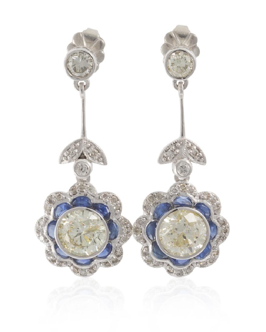 A pair of diamond and sapphire earrings: 18k white gold Centering two round brilliant-cut diamonds totaling 2.03 cts. and graded M+ color, SI-I clarity surrounded by sixteen caliber-cut sapphires and fifty-six full-cut round diamonds totalin