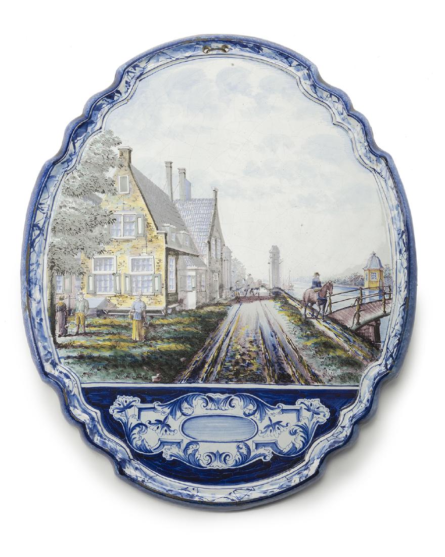 A hand-painted Delft-style pottery wall plaque: Fourth quarter 19th century, Danish Signed to verso: LA Polychrome with scalloped blue edge depicting shorefront houses and a rider on horseback, the lower portion with a painted armorial style plaque