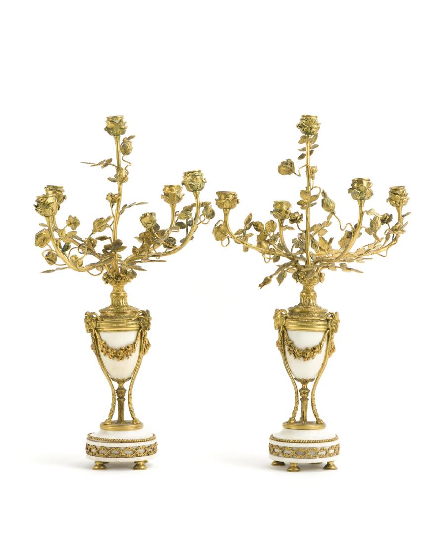 A pair of Louis XVI-style candelabra: Late 19th/early 20th century Each gilt-bronze mounted white marble urn flanked by rams heads and issuing a five-light candelabrum, 2 pieces Each: 23.5" H x 15" W x 14.75" D