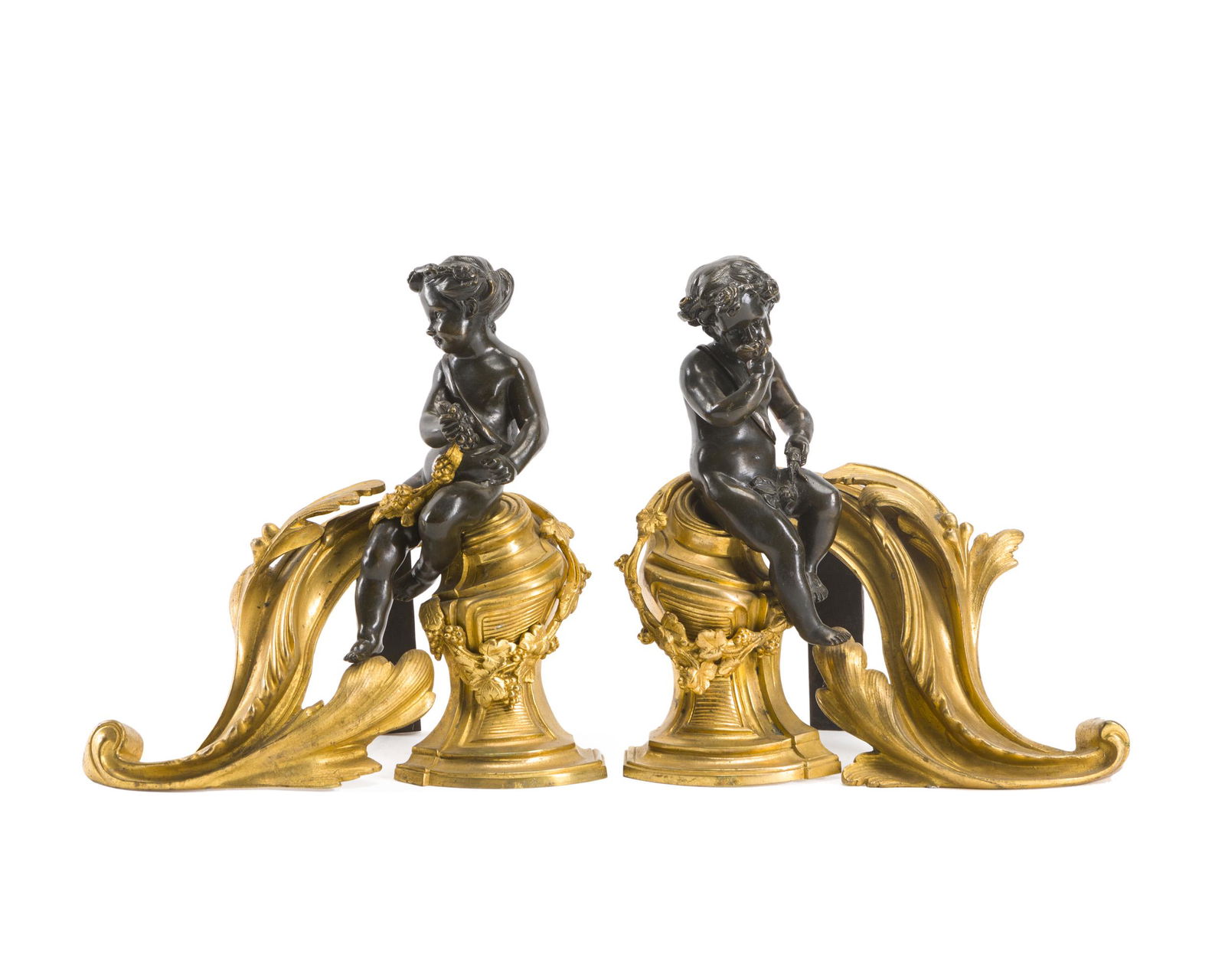 A pair of gilt-bronze chenets: Late 19th/early 20th century Each set with opposing patinated bronze putti enjoying wine and grapes seated on a scrolled gilt-bronze base adorned with garlands of gilt-bronze flowers, 2 pieces Each