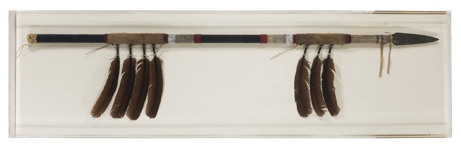 An acrylic cased spear: Contemporary Mounted to a linen backing within an acrylic case, the beaded shaft with dyed feathers Overall: 20.25" H x 72.25" W x 3.75" D
