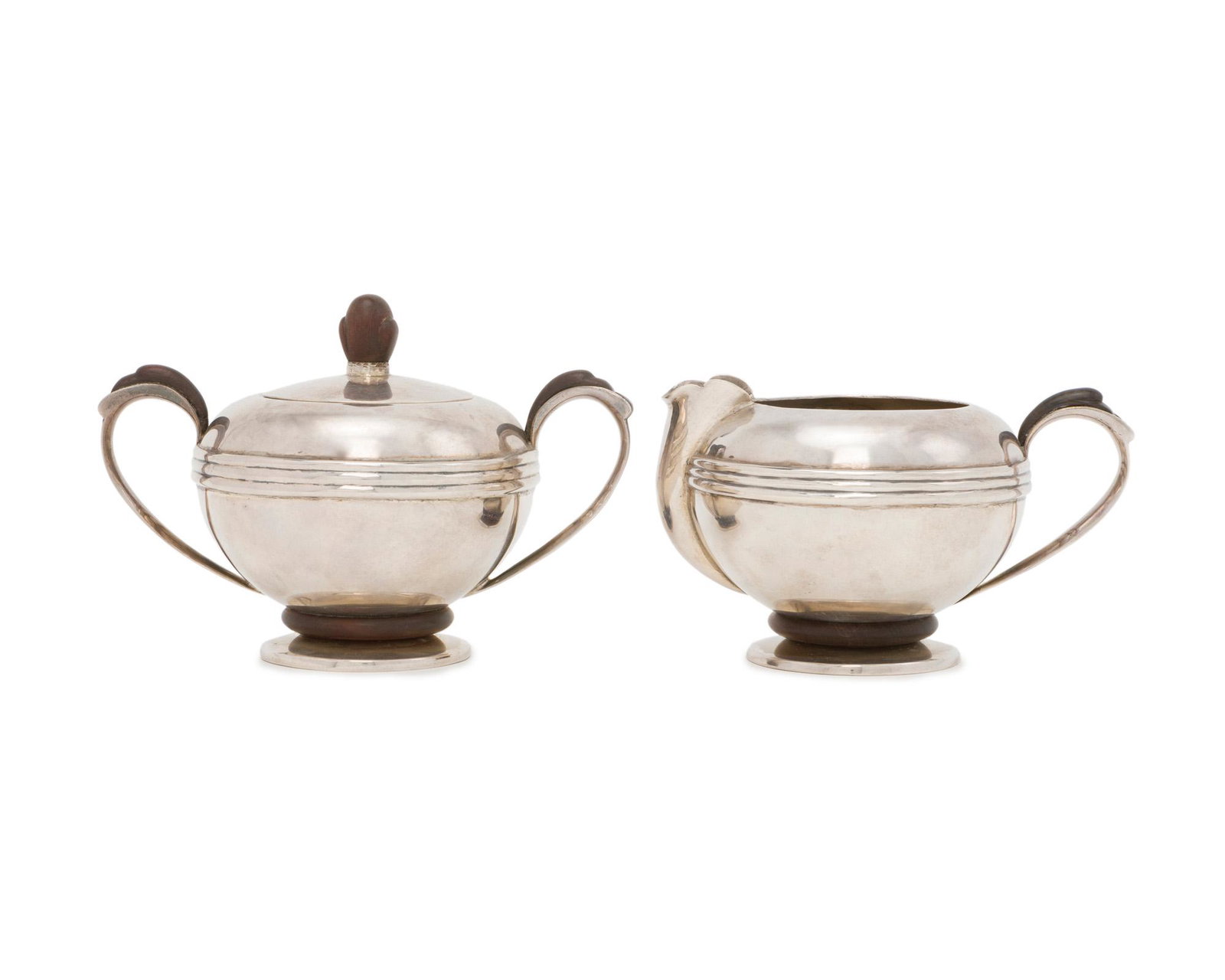 A William Spratling rosewood and sterling silver cream: 1945-1946; First Design Period; Taxco, Mexico Each stamped for William Spratling; Further stamped: Sterling Each smooth silver body with applied silver stripes issuing carved rosewood handles and furt