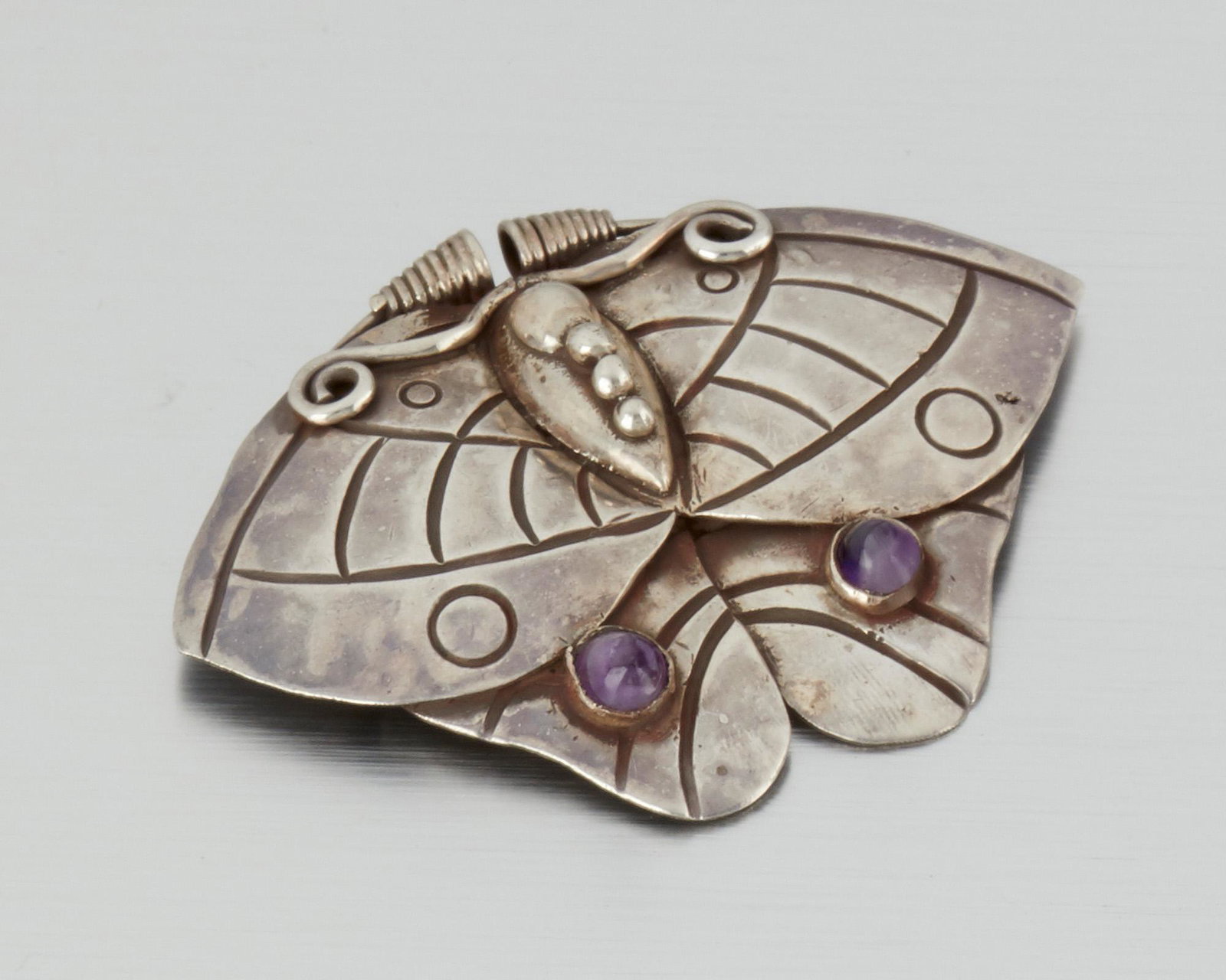 A William Spratling silver and amethyst moth brooch: 1940-1946; First Design Period; Taxco, Mexico Stamped for William Spratling; Further stamped: Made in Mexico / Silver Designed as a stylized moth with two inset cabochon amethyst stones 2.125" H x 2.8