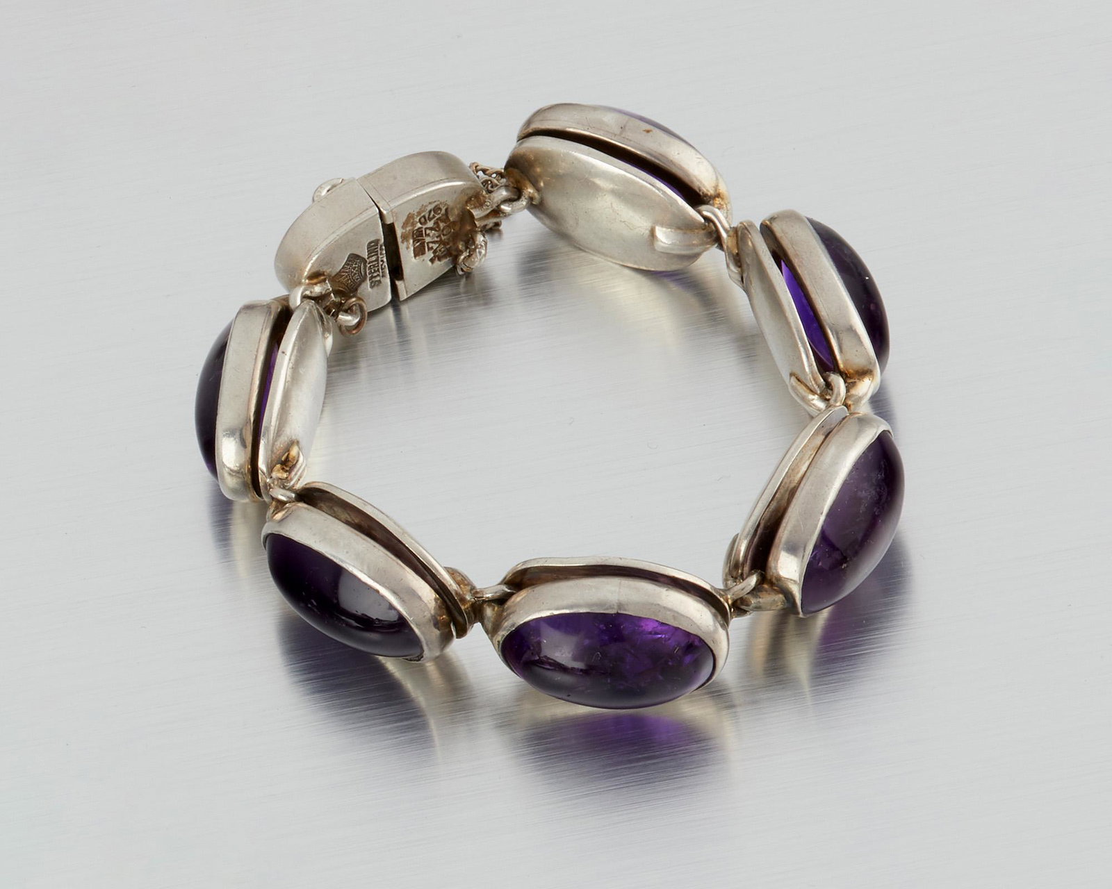An Antonio Pineda silver and amethyst bracelet: 1953-1979; Taxco, Mexico Crown mark for Antonio Pineda; Eagle 17; Further stamped: Sterling / Mexico / Silver / 970 / ZZ694 The oval cabochon amethyst links raised over silver backings 6.75" W x .625"