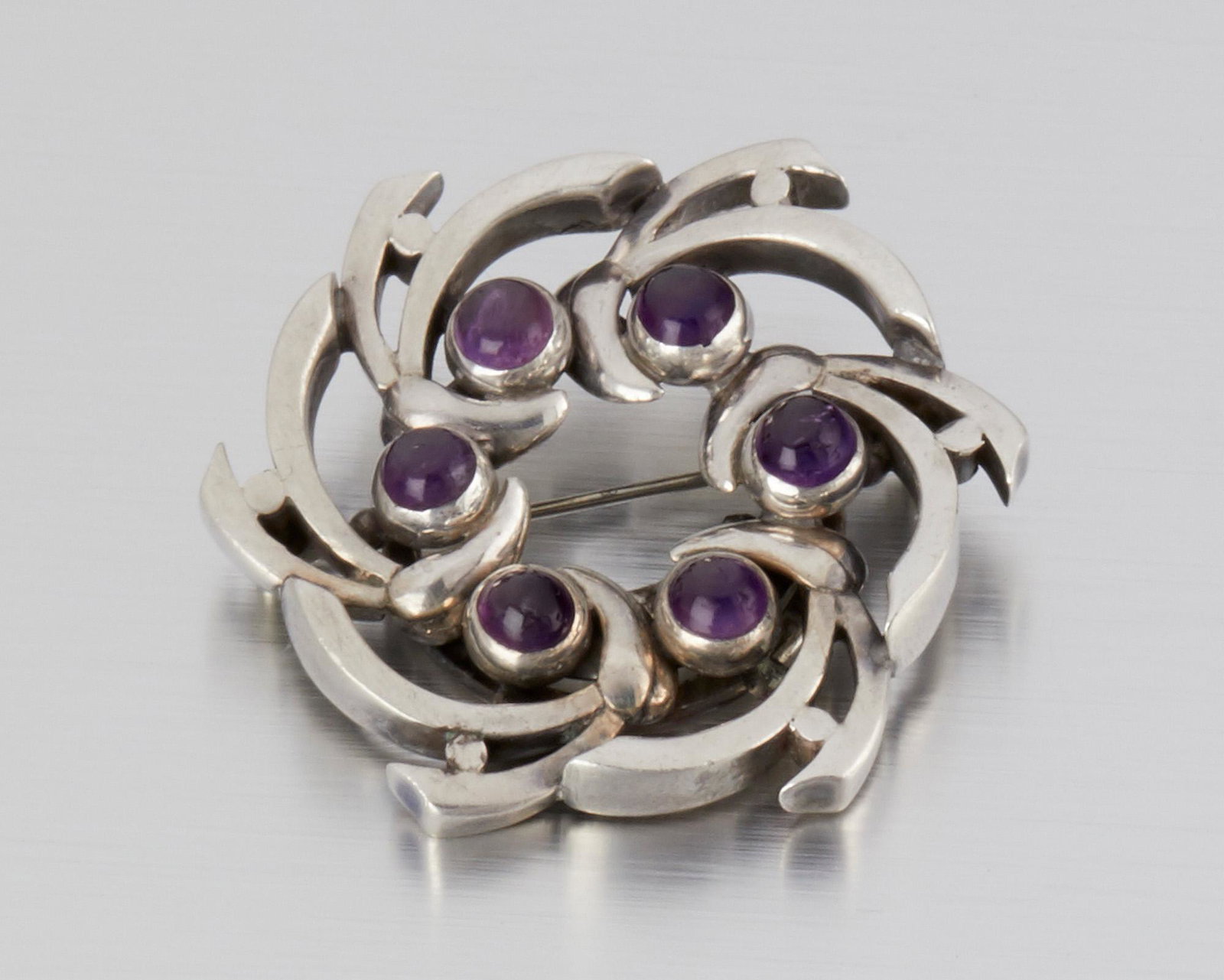 An Antonio Pineda silver and amethyst brooch: 1953-1979; Taxco, Mexico Crown mark for Antonio Pineda; Eagle 17; Further stamped: Hecho en Mexico / Silver / 970 The spray brooch formed from the letter "A" set with six round amethyst cabochons 2" D