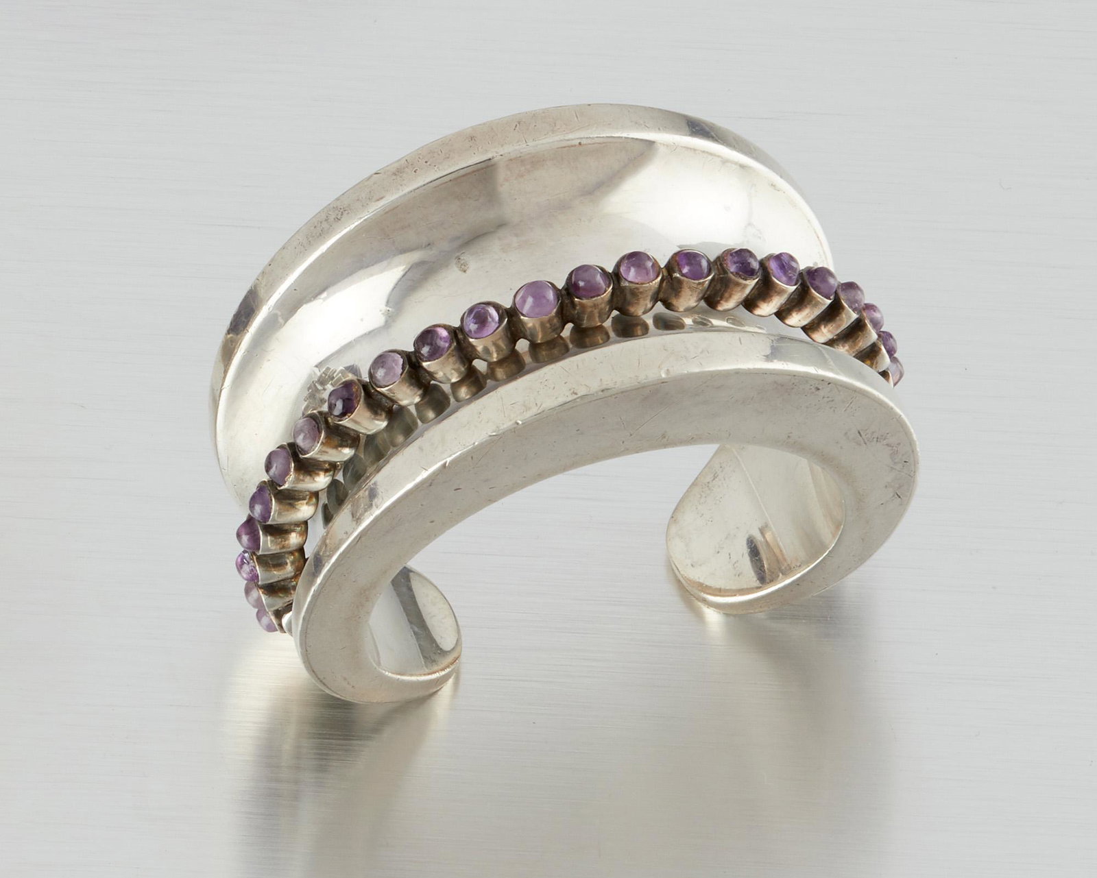 An Antonio Pineda silver and amethyst bracelet: 1953-1979; Taxco, Mexico Crown mark for Antonio Pineda; Eagle 17; Further stamped: Hecho en Mexico / Silver / 970 / ZZ529 The concave cuff bracelet with raised amethyst cabochons in a kinetic setting 
