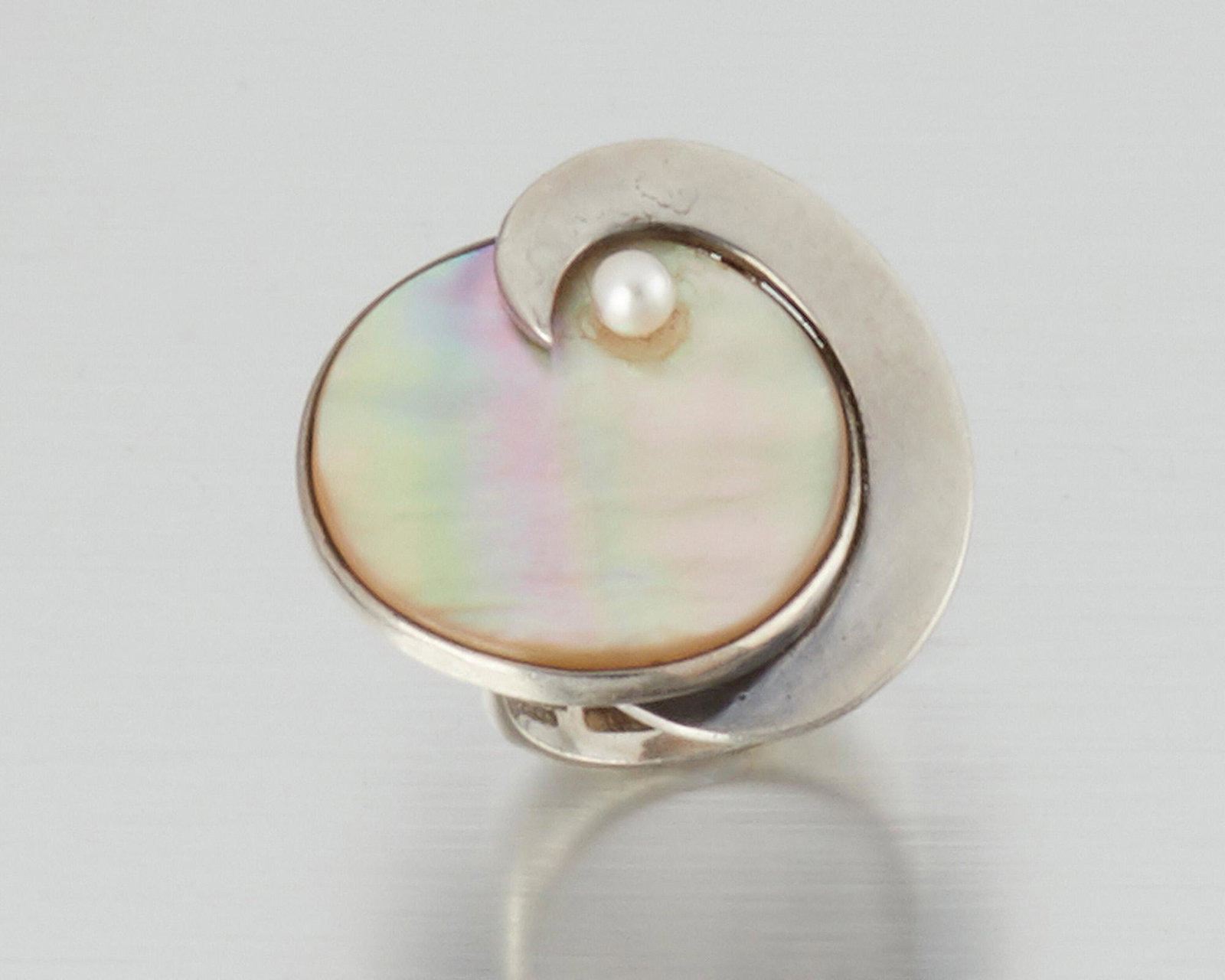 An Antonio Pineda sterling silver and gem-set ring: 1953-1979; Taxco, Mexico Crown mark for Antonio Pineda; Eagle 17; Further stamped: Sterling / Silver / Mexico The mother-of-pearl disc with silver crescent design topped with a single cultured pearl R